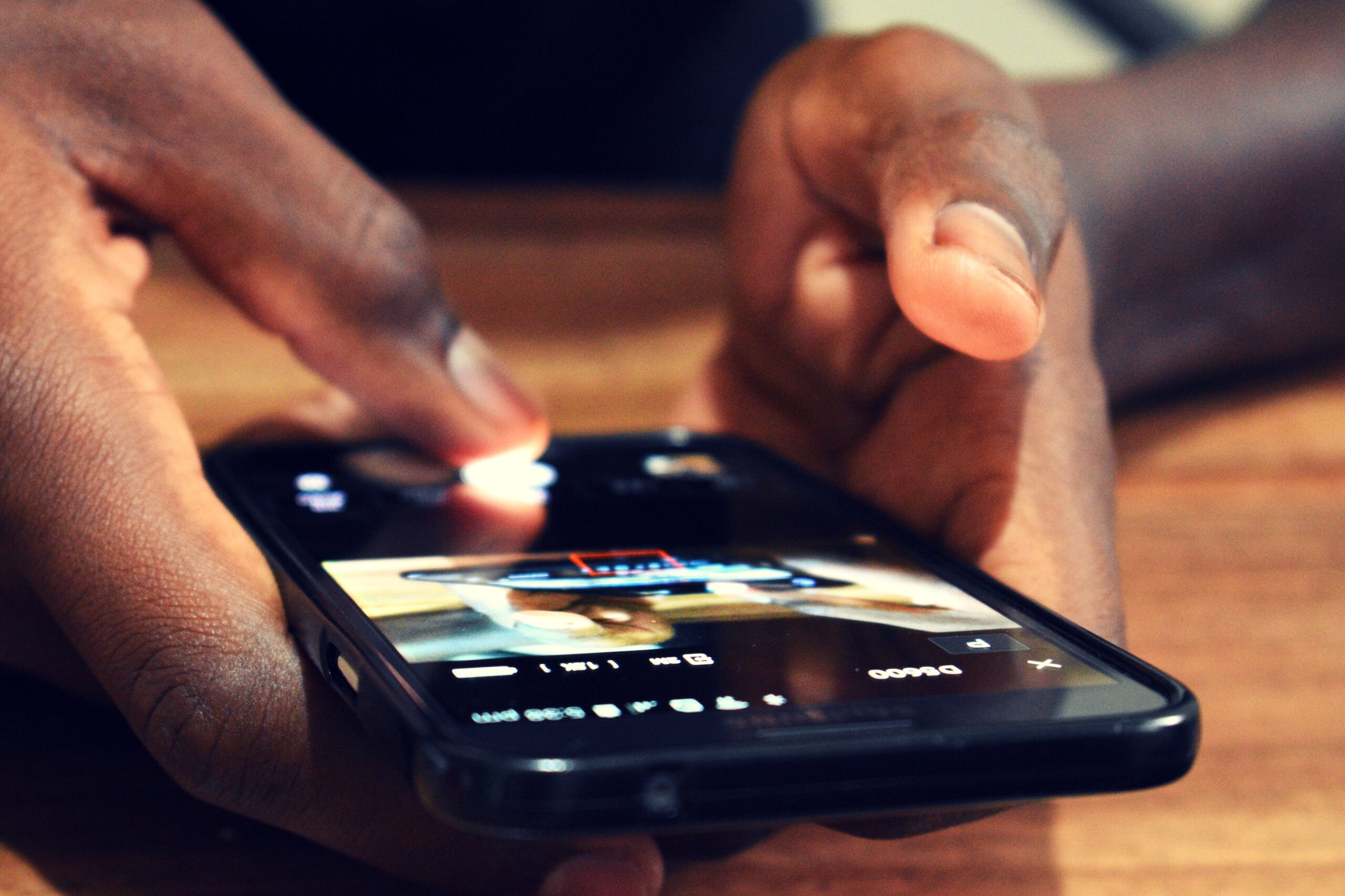 A black person's hand's hold a smartphone over a wooden table